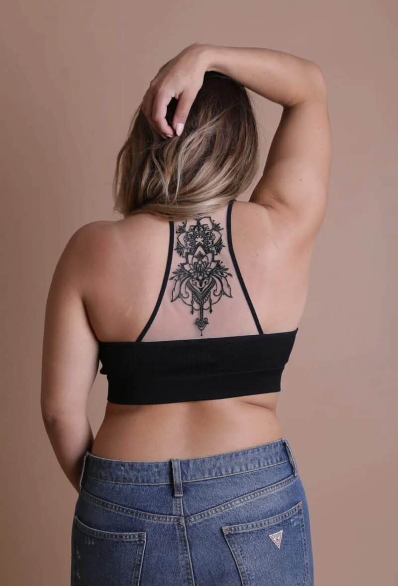 Woman showing off a back tattoo while wearing jeans and a black top.