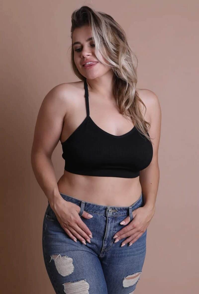 Woman in a black top and ripped jeans posing with hands on waist.