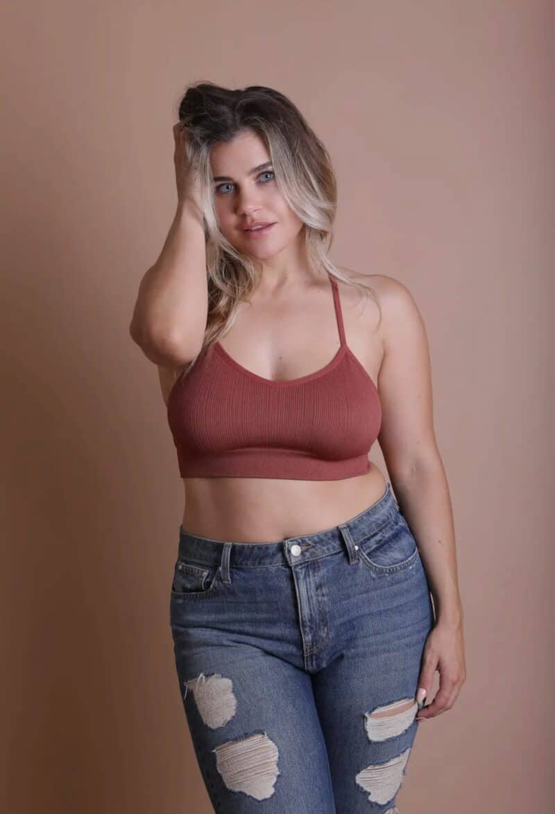 Woman posing in a maroon crop top and ripped jeans against a tan background.