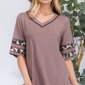 Woman modeling a casual taupe top with lace details and a sun hat.