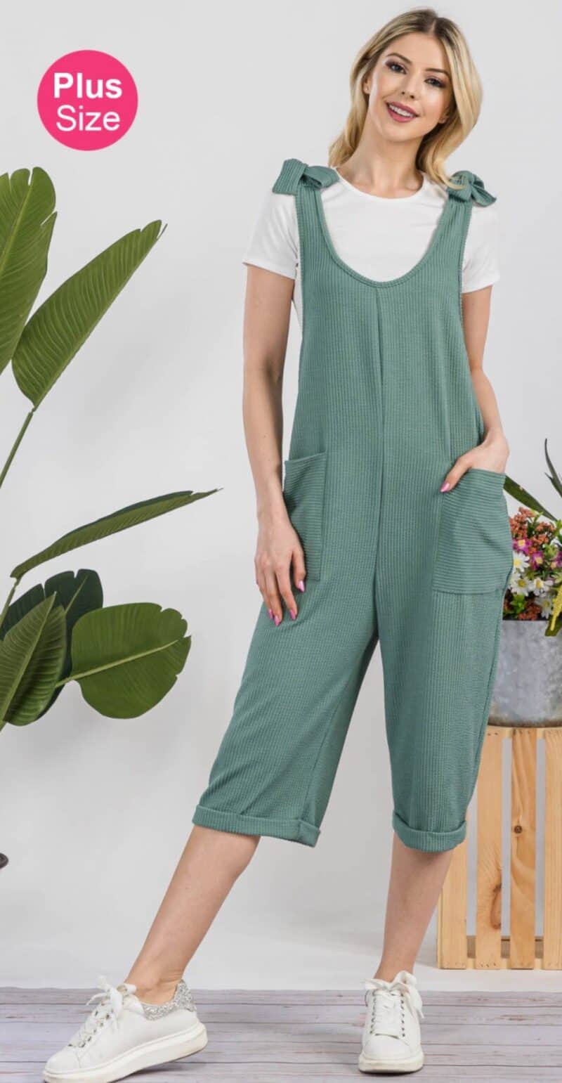 Woman posing in a green plus-size jumpsuit with white sneakers.