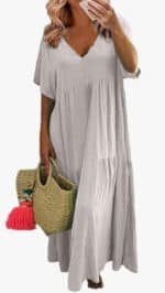 A woman wears the linen dress holds a woven straw bag with pink tassels.