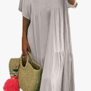 A woman wears the linen dress holds a woven straw bag with pink tassels.